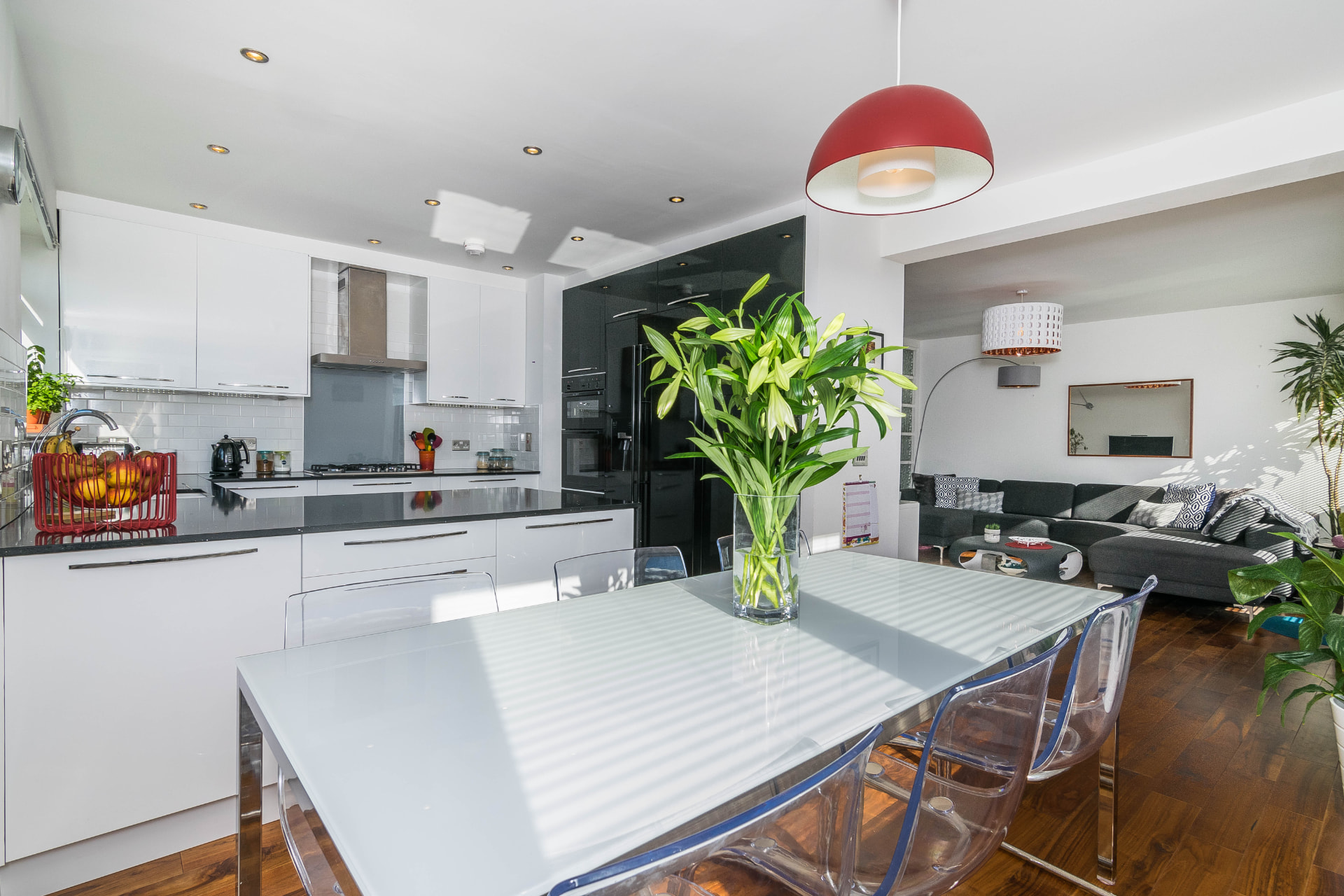 Open-plan dining kitchen at Mortonhall Road with white and black cabinets, a glass dining table, clear chairs and a red pendant light.