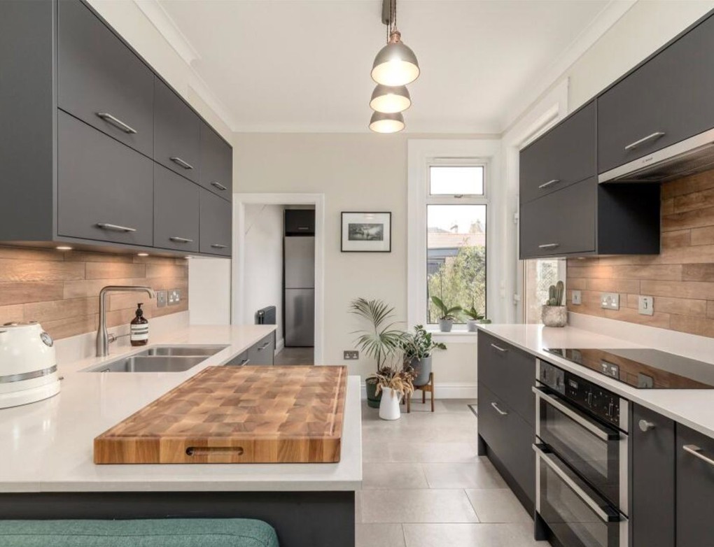 Dark grey kitchen at Warriston Grove with white worktops, wood-effect splashbacks, a peninsula and green upholstered bench seating.