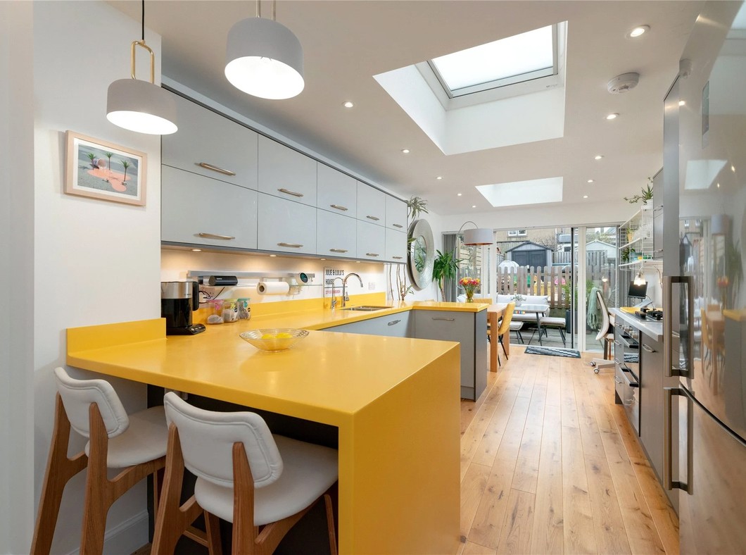 Kitchen at West Savile Terrace with yellow worktops and breakfast bar, grey cabinets, rooflights and glazed doors to the garden.